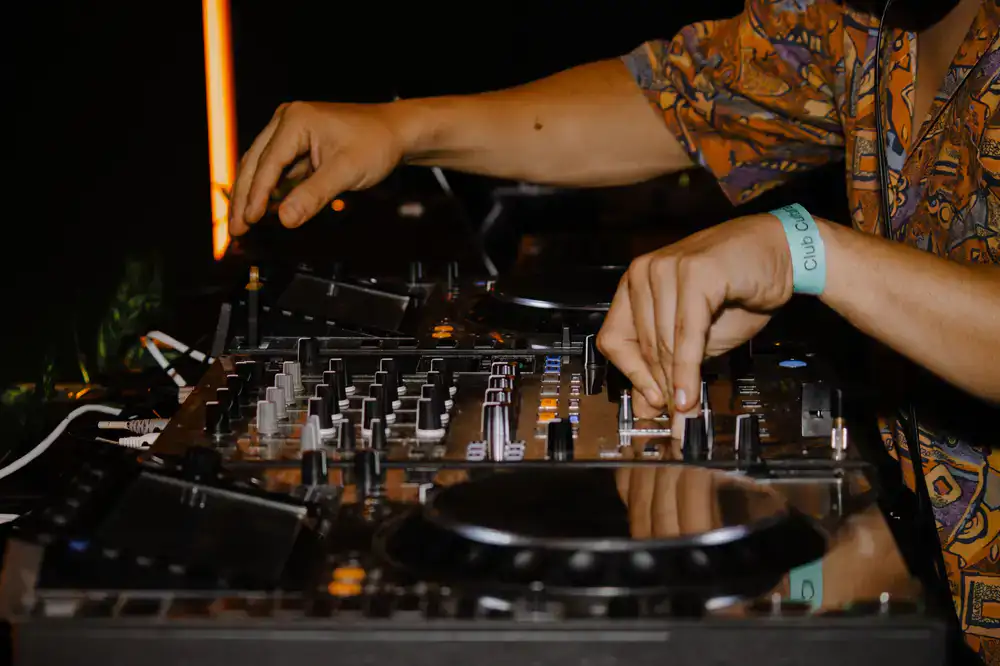 Hands operating a brightly lit DJ and turntable rhythm arcade cabinet